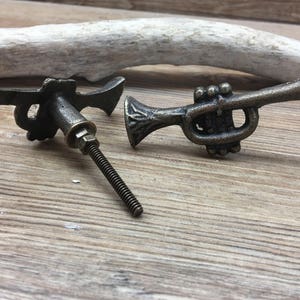 May include: Two antique bronze-effect trumpet-shaped cabinet knobs. One is assembled with a threaded bolt, the other disassembled. The knobs are designed to resemble miniature trumpets, adding a musical touch to furniture, with a vintage aesthetic.