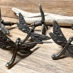 May include: Four antique bronze dragonfly drawer pulls with intricate details. The pulls are designed to resemble dragonflies with wings, bodies, and legs.