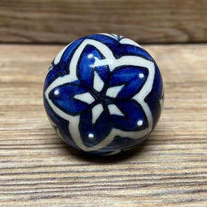 May include: A white ceramic sphere with a blue and white floral design. The sphere has a glossy finish and is decorated with a repeating pattern of blue flowers with white centers.