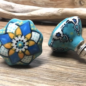 May include: Two ceramic cabinet knobs with a blue, yellow, and white floral design. One knob has a screw attached.