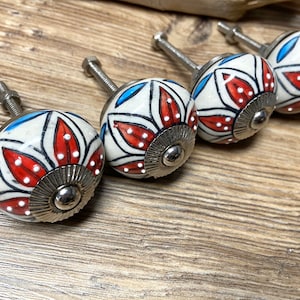 Op de afbeelding: Vier decoratieve keramische kastknoppen met een bloemmotief in rood, wit en blauw. Elke knop heeft een zilverkleurige basis en schroef. De knoppen zijn gerangschikt op een houten oppervlak.