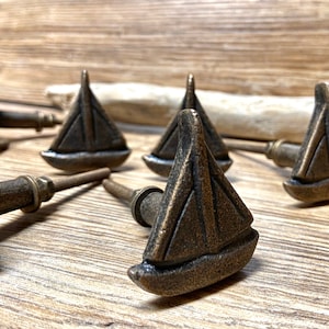 以下が含まれることがあります： ブロンズトーンのヨット型キャビネットノブ。ノブは、テクスチャード加工が施された詳細なヨットのデザインが特徴です。このハードウェアは家具用に設計されており、どんな部屋にも航海をテーマにした雰囲気を加えます。