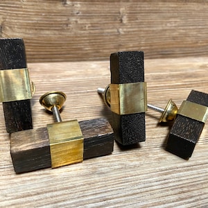 Pode incluir: Conjunto de quatro puxadores retangulares de madeira escura, com faixas de metal cor de latão. Cada puxador tem um parafuso e uma cabeça decorativa cor de latão. Os puxadores estão dispostos sobre uma superfície de madeira.