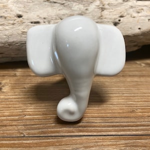 May include: A white ceramic elephant figurine with large ears and a curled trunk. The elephant is glossy and smooth, with a simple, elegant design. The figurine is a decorative item.