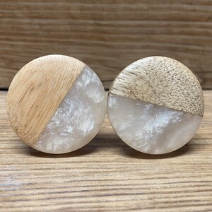 May include: A pair of circular ear plugs featuring a split design with one half made of light-toned natural wood and the other half made of a translucent, pearlescent white resin material with a swirling, marbled texture throughout the surface.