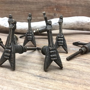 May include: A selection of bronze-toned guitar-shaped cabinet knobs. The knobs feature detailed strings and fretboards, with a distressed finish. These furniture fittings offer a unique, musical aesthetic, suitable for any room.