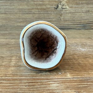 Op de afbeelding: Een decoratieve keramische knop met een geode-ontwerp. De knop heeft een lichtblauwe buitenkant, een goudkleurige rand en een donkerbruin, getextureerd interieur. Een decoratief element voor meubels.