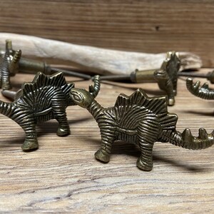 Op de afbeelding: Set van vijf antieke gouden trekknoppen in de vorm van een dinosaurus. De knoppen zijn gedetailleerd met textuur en hebben een vintage uitstraling.