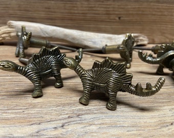 May include: Set of five antique gold dinosaur-shaped drawer pulls. The pulls are detailed with textured scales and have a vintage look.