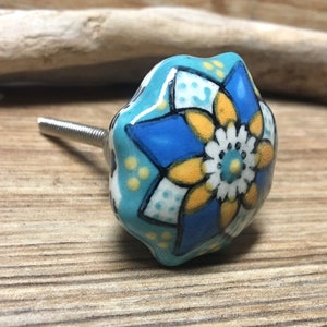 Può includere: Un pomello in ceramica blu e giallo con un motivo floreale. Il pomello ha una vite argentata.