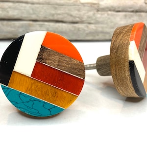 以下が含まれることがあります： 丸くカラフルなデザインの装飾的なキャビネットノブ2つ。ノブは、木材、黒、白、オレンジ、黄色、赤、ターコイズなど、さまざまな素材と色を組み合わせています。各ノブは木製のベースと金属製のネジが付いています。