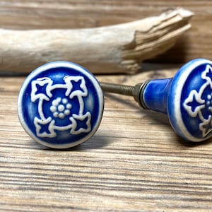 Könnte beinhalten: Zwei blaue und weiße Keramik-Schrankknöpfe mit floralem Design. Die Knöpfe haben eine runde Form mit einem dekorativen Muster und einer Metallschraube. Diese Knöpfe sind perfekt, um jedem Möbelstück einen Hauch von Eleganz zu verleihen.