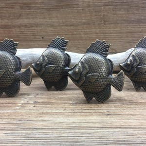 May include: Four antique-style metal fish drawer pulls in a dark bronze finish. The fish are detailed with scales and fins.