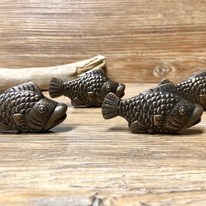May include: Four antique bronze fish-shaped cabinet knobs. The knobs are detailed with scales and have a realistic fish design.