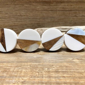 以下が含まれることがあります： 丸い白と木製のプラグが4つ。対角線上に木がはめ込まれています。木は濃い茶色です。一部のプラグには真珠光沢のある象嵌細工があります。プラグは木製の表面に表示されています。