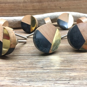 Peut inclure: Ensemble de boutons de meubles décoratifs. Chaque bouton présente un design circulaire avec des segments de bois, de noir et de métal doré. Les boutons sont fixés à des vis argentées et sont présentés sur une surface en bois.