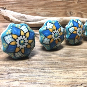 May include: Four ceramic knobs with a blue, yellow, and white floral design. The knobs have a starburst shape and are perfect for adding a touch of color and style to any room.