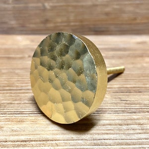 Puede incluir: Pomo de armario dorado con acabado martillado. Tiene una cara redonda y un vástago cilíndrico. La superficie es texturizada, para muebles.