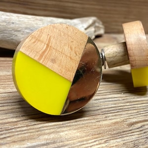 May include: A decorative bottle stopper with a round, segmented design. It features light wood, a shiny metallic section, and a vibrant yellow accent. The cork base also has a yellow section.