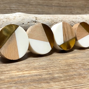 May include: Four circular cabinet knobs with a contemporary design. Each knob combines light wood, white, and gold-coloured metal. The knobs are arranged in a row, highlighting their geometric pattern and contrasting materials.