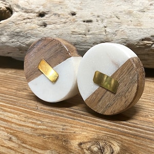 May include: Two round wooden cabinet knobs with a white marble inlay and a gold-colored metal accent. The knobs are made of wood and marble, and are set against a wooden background.