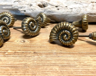Peut inclure: Un ensemble de boutons de cabinet en or antique en forme de coquilles d'ammonites. Les boutons ont un design en spirale détaillé et sont parfaits pour ajouter une touche de charme côtier à n'importe quelle maison.