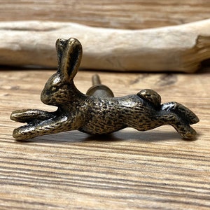 May include: A bronze-colored rabbit figurine door knob with a detailed design. The rabbit is in a running position with its ears perked up.