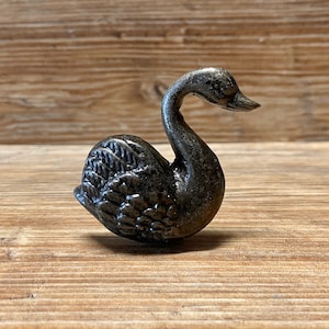 Könnte beinhalten: Eine schwarze Metallschwanenfigur mit detaillierten Federn. Der Schwan sitzt mit dem Kopf zur Seite gedreht.