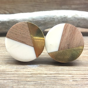 以下が含まれることがあります： モダンなデザインの丸いキャビネットノブが2つ。各ノブは、白、明るい茶色の木材、金色の金属の組み合わせが特徴です。ノブは木製の表面に配置されています。