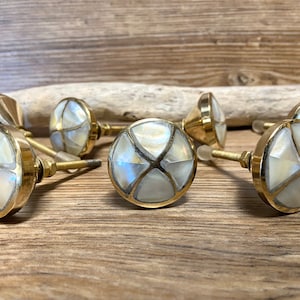 May include: A selection of round cabinet knobs with a brass finish and inlaid mother-of-pearl design. The knobs are displayed on a wooden surface, highlighting their decorative nature. The knobs have a diameter of approximately 3.8 cm.