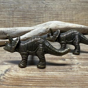 Op de afbeelding: Twee bronzen dino-vormige kastknoppen. De dinosaurussen staan in een looppose met hun staarten omhoog.