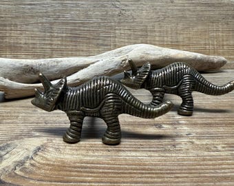 May include: Two bronze-colored dinosaur-shaped cabinet knobs. The dinosaurs are in a walking pose with their tails raised.