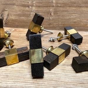 Pode incluir: Um conjunto de puxadores de armário de madeira castanha escura com detalhes em metal cor de latão. Cada puxador tem formato retangular com uma faixa de latão no centro e um parafuso para instalação. Dispostos sobre uma superfície de madeira.