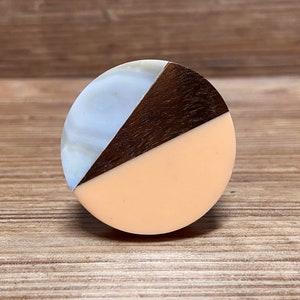 Pode incluir: Um puxador de armário redondo com um design segmentado. O puxador apresenta uma seção azul claro e branco, uma seção de madeira marrom escuro e uma seção cor de pêssego. Para gaveta ou armário.