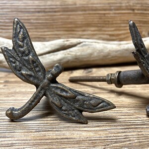 May include: Two antique bronze dragonfly drawer pulls with a detailed design. The pulls have a screw-on attachment.