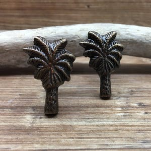 May include: Two antique bronze palm tree shaped drawer pulls. The pulls have a detailed design and are perfect for adding a tropical touch to any home decor.