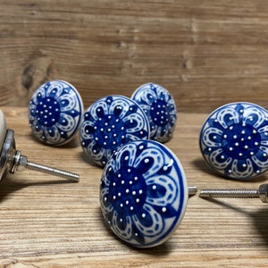 May include: Six blue and white ceramic drawer knobs with a floral design. The knobs have a silver screw attachment.