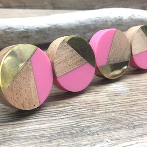 May include: Four circular cabinet knobs featuring a segmented design of natural light wood, polished gold-tone metal, and solid pink resin. Each knob has a threaded metal bolt extending from the back for installation on furniture or cabinetry.