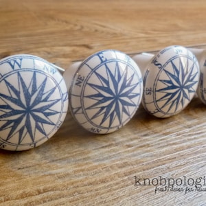 May include: Four white ceramic cabinet knobs with a blue compass rose design. Each knob features a compass rose with the cardinal directions marked in blue.