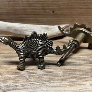 Op de afbeelding: Twee bronzen dinosaurus-ladegrepen met een schroefontwerp. De dinosaurus is een stegosaurus met een gedetailleerd, getextureerd lichaam.