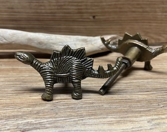 May include: Two bronze dinosaur drawer pulls with a screw-on design. The dinosaur is a stegosaurus with a detailed textured body.