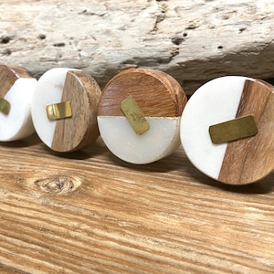 May include: Four decorative cabinet knobs. Each knob is a half-circle of light wood and a half-circle of white material, with a rectangular brass accent. The knobs are arranged on a wooden surface.