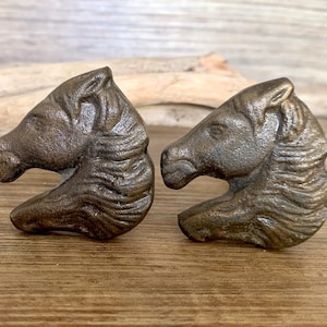 May include: Two antique bronze horse head drawer pulls. The horse heads are facing opposite directions and have a detailed mane and face.