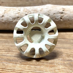 May include: White metal cabinet knob with a circular design and a decorative, openwork pattern. The knob has a slightly raised center and a smooth, matte finish.