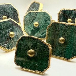 Op de afbeelding: Een verzameling decoratieve kastknoppen. Elke knop heeft een donkergroene, onregelmatig gevormde steen met goudkleurige randen en een messingkleurige middenknop. De knoppen zijn gerangschikt op een witte ondergrond.