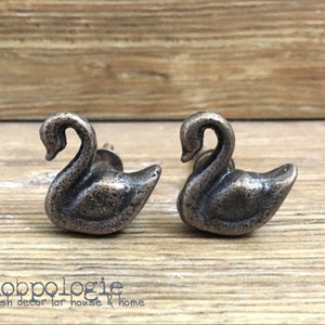 May include: Two antique silver swan-shaped drawer pulls. The pulls have a distressed finish and are perfect for adding a touch of rustic charm to any home.
