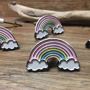 Puede incluir: Pomos de armario con forma de arcoíris, con colores rosa, amarillo, azul y blanco. Cada pomo tiene un contorno negro y detalles de nubes blancas. Estos pomos metálicos están diseñados para muebles.