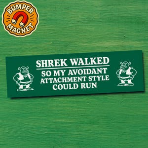 Könnte beinhalten: Grüner Stoßstangenmagnet mit weißem Text: "SHREK WALKED SO MY AVOIDANT ATTACHMENT STYLE COULD RUN". Cartoon-Shrek-Bilder flankieren den Text. Ein runder Magnet mit "BUMPER MAGNET" befindet sich in der oberen linken Ecke.