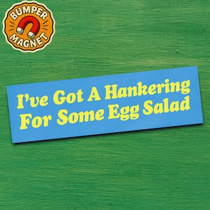 May include: A blue bumper sticker with the text "I've Got A Hankering For Some Egg Salad" in yellow. A round magnet with the words "Bumper Magnet" and a magnet graphic is in the upper left corner. The background is green.