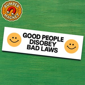 May include: A white bumper sticker with the text "GOOD PEOPLE DISOBEY BAD LAWS" in black, flanked by yellow smiley faces. A round magnet with a magnet graphic is in the upper left corner. The background is a green surface.